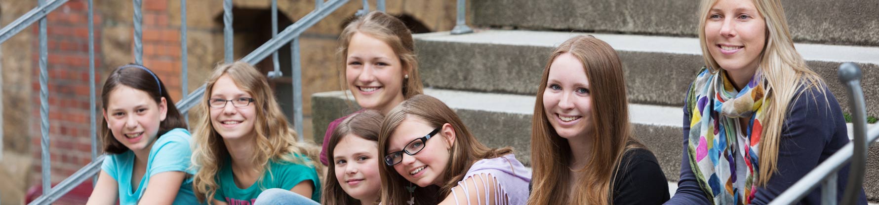 Eine Gruppe Mädchen sitzt auf dem Schulhof auf einer Treppe und lacht in die Kamera