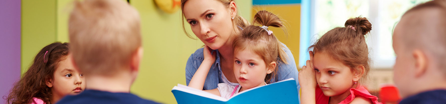Eine Erzieherin sitzt mit Kindern im Kreis uns liest ihnen aus einem Buch vor