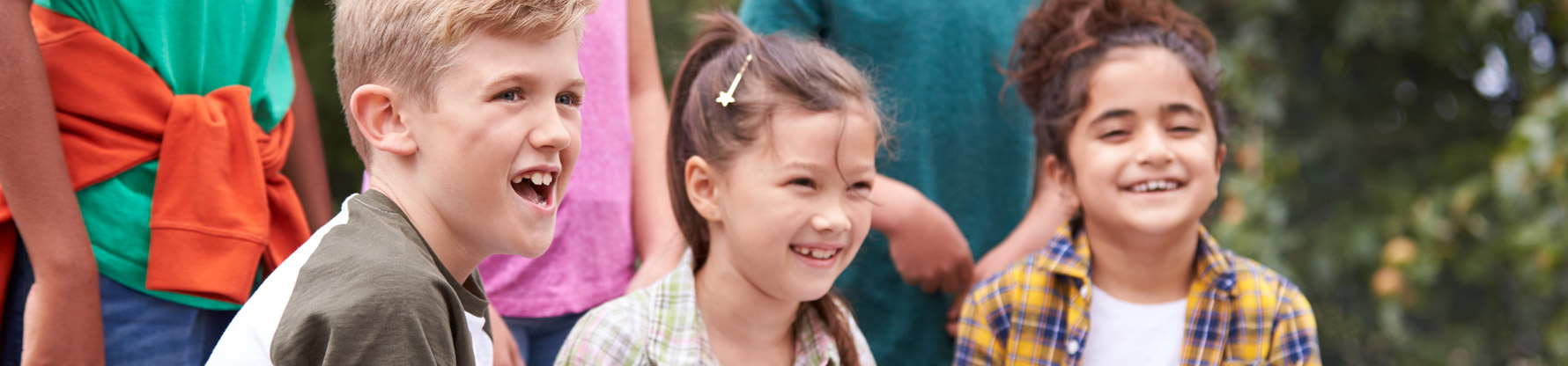 Ein Junge und zwei Mädchen schauen anderen Kindern beim Spielen zu