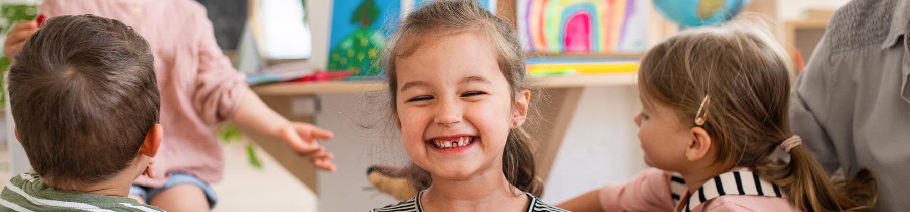 Ein Mädchen mit Zahnlücke grinst in die Kamera während die anderen Kinder im Hintergrund spielen